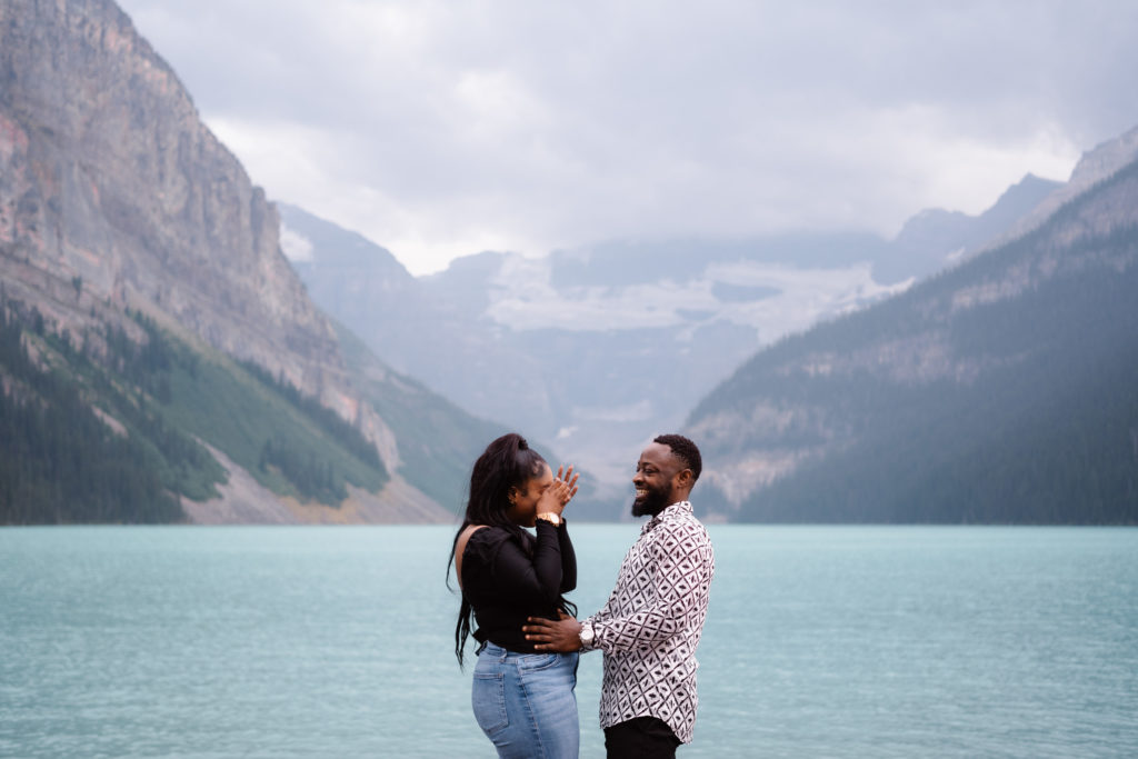 Newly engaged couple wipe tears away in front of Lake Louise.