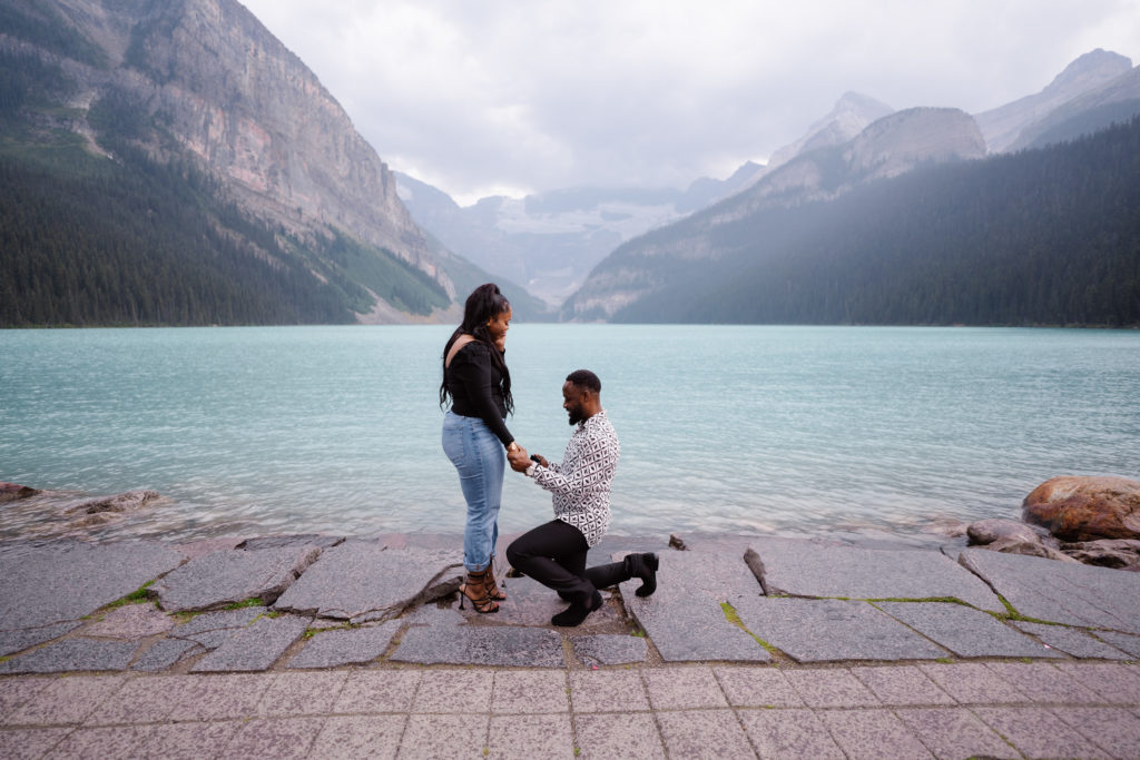 Man slides ring on womans finger during Lake Louise Proposal.