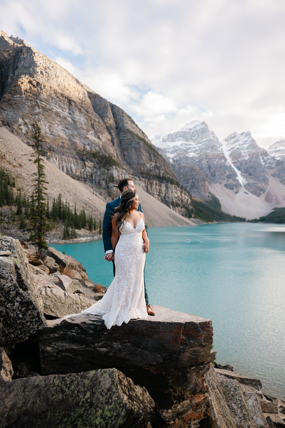 Bride and groom hold hands and look out over sunset at Moraine Lake