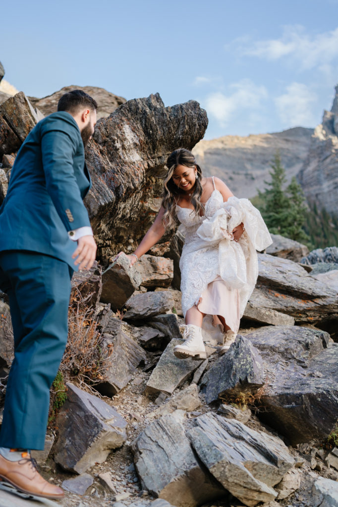 Bride navigates the rockpile at moraine lake in a lace dress and hiking boots. 