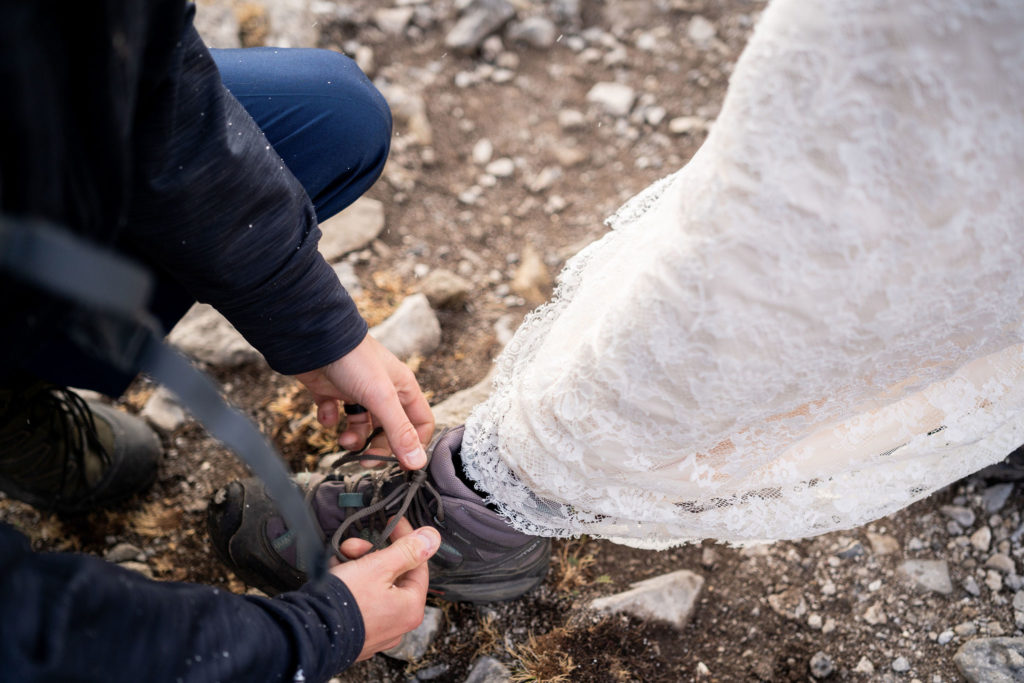 groom bends down to tie brides hiking boot up
