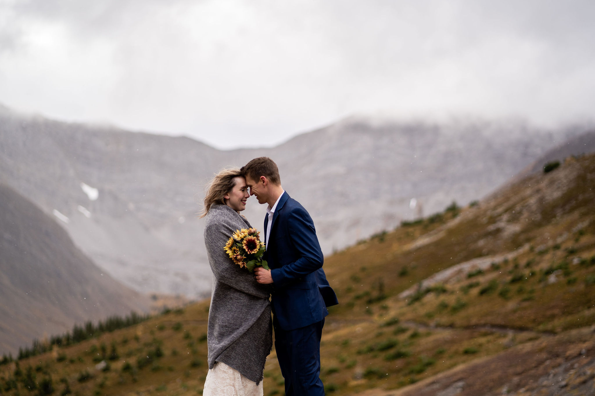 bride and groom hold bouquet of sunflowers on Ptarmigan Cirque in Kananaskis. 