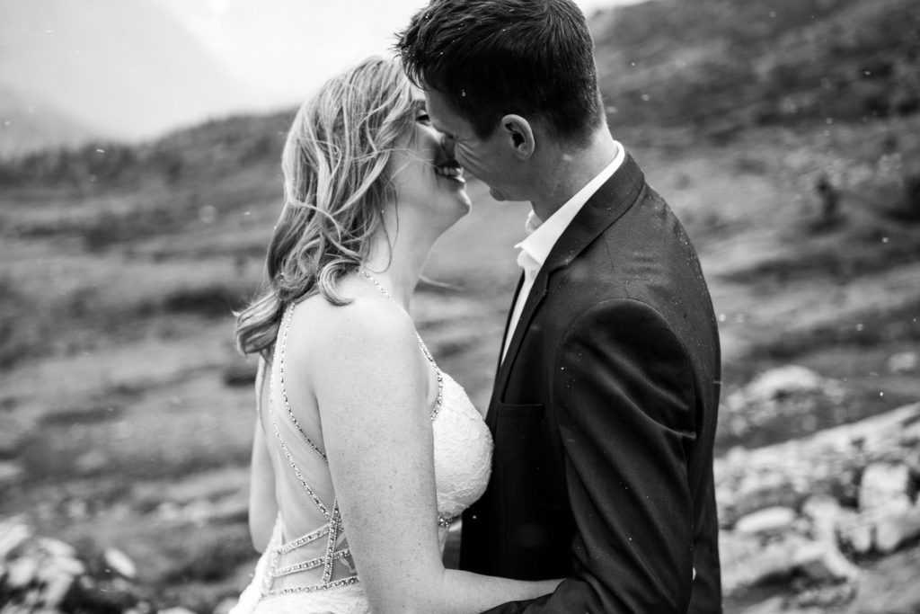 Black and white photo of bride and groom kissing as snow falls. 