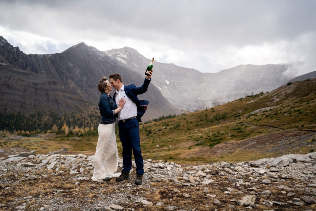 Groom holds up bottle of champagne on Ptarmigan Cirque