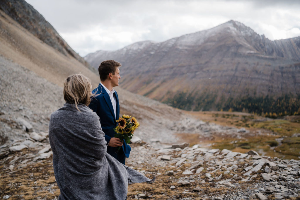 Groom in blue suit holds sunflowers during Kananaskis hiking elopement