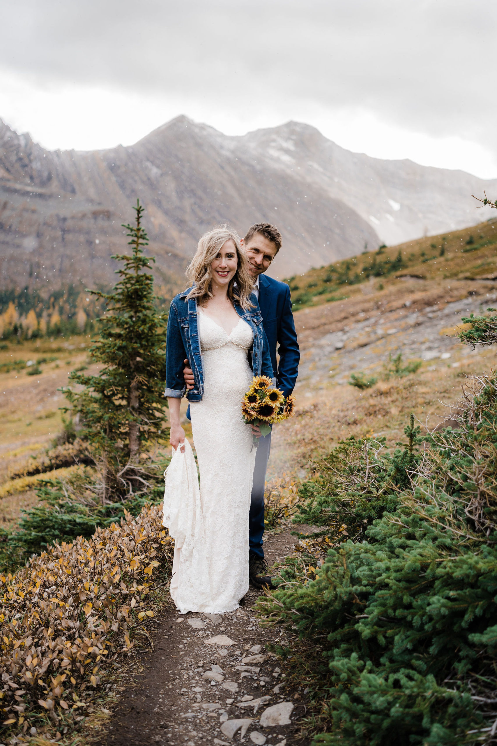 bride and groom smile at camera while the snow falls on them in Kananaskis