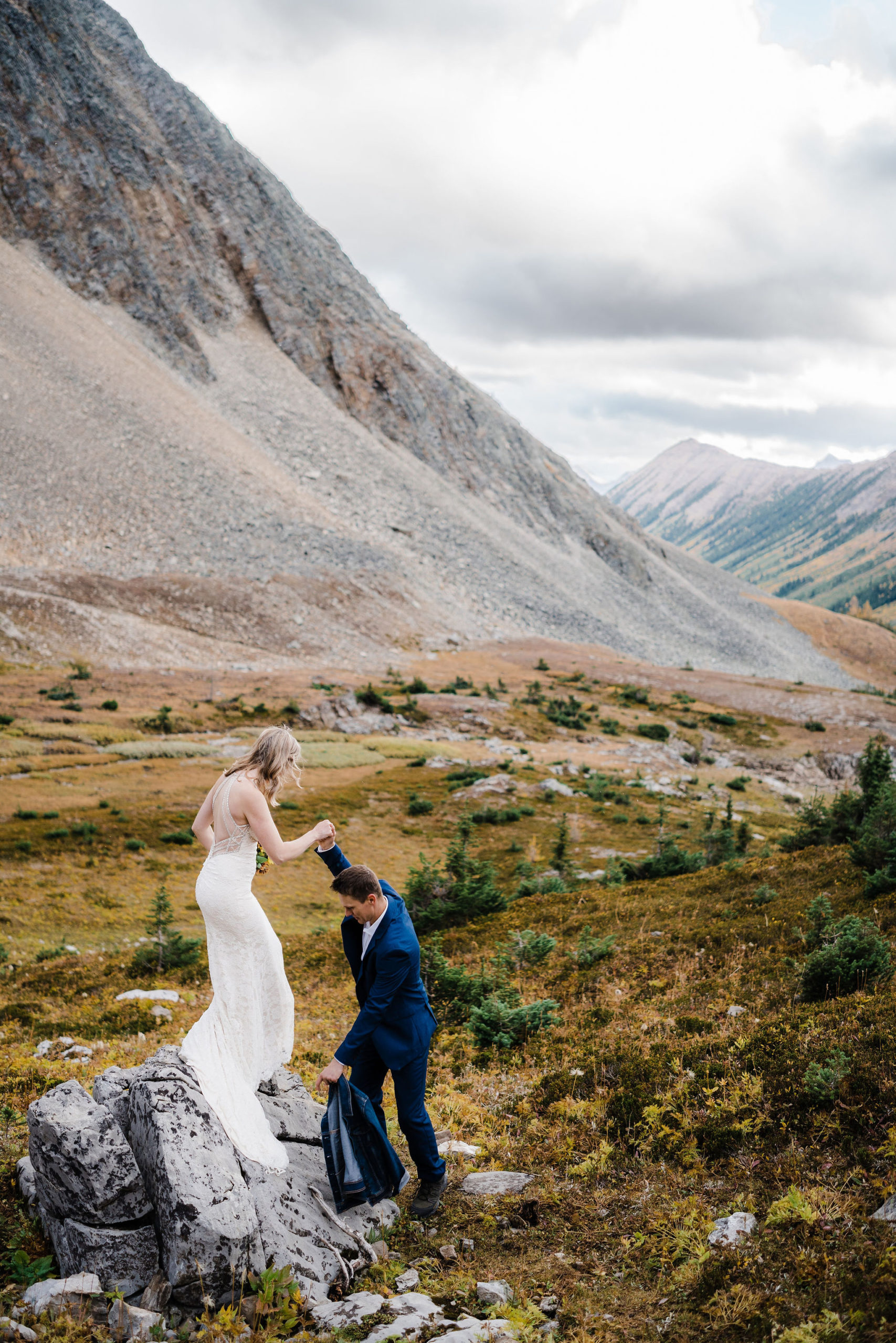 Groom helps bride down off rock in Kananaskis hiking elopement