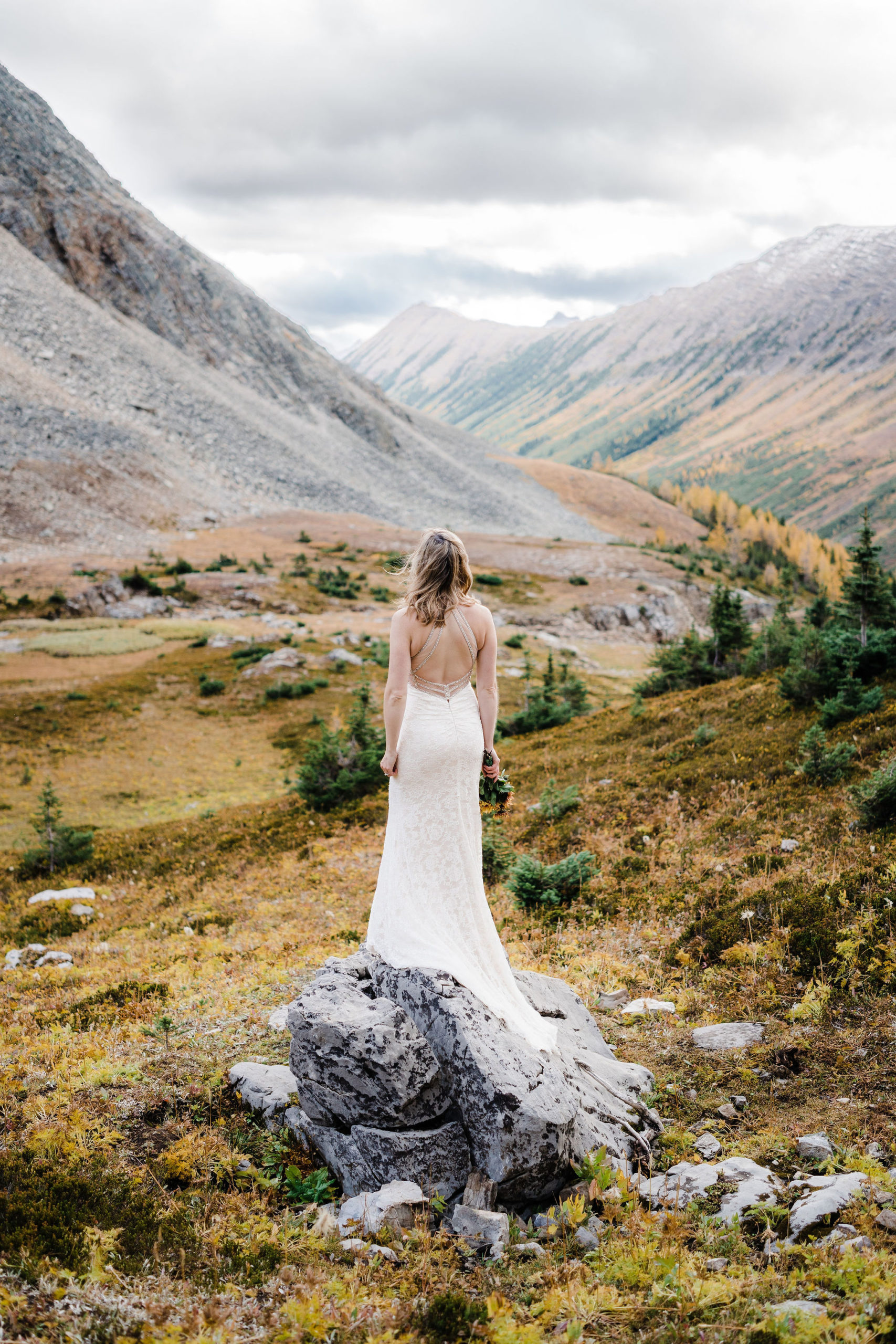 Bride stands on rock while looking down the valley at Ptarmigan Cirque in Kananaskis hiking elopement