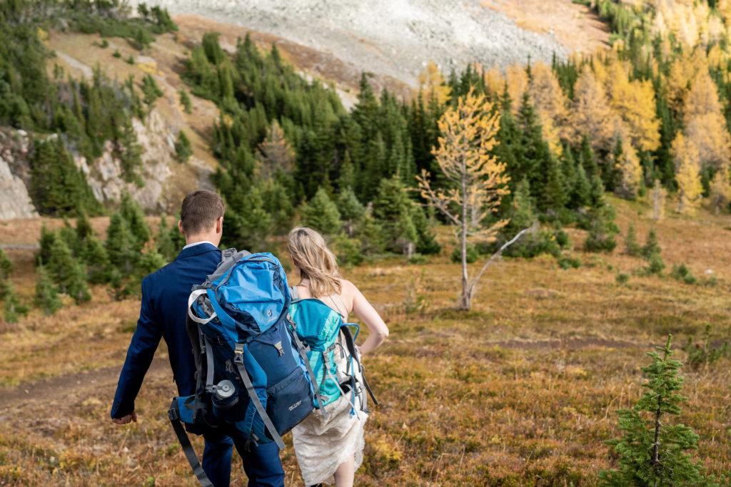 bride and groom walk down trail while the larch trees are yellow behind them