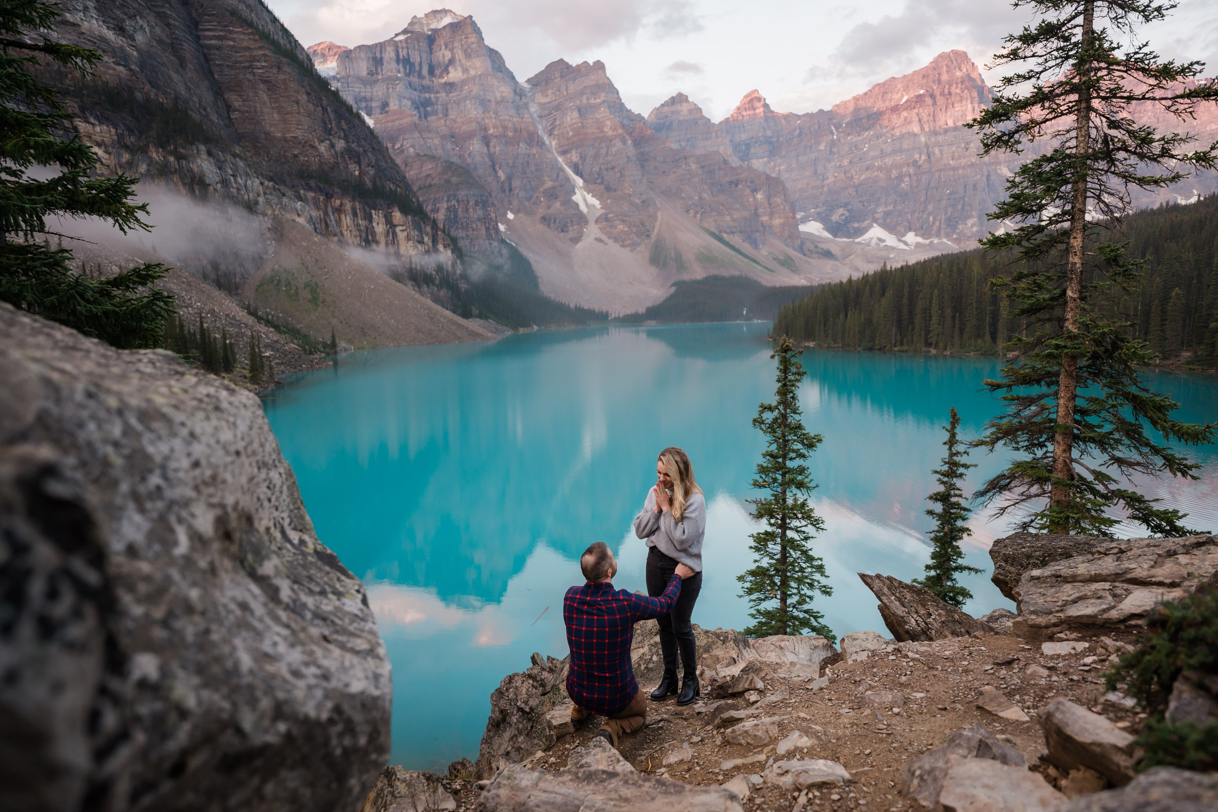 Banff surprise proposal as girl covers her mouth in surprise as boyfriend kneels down in front of her. 