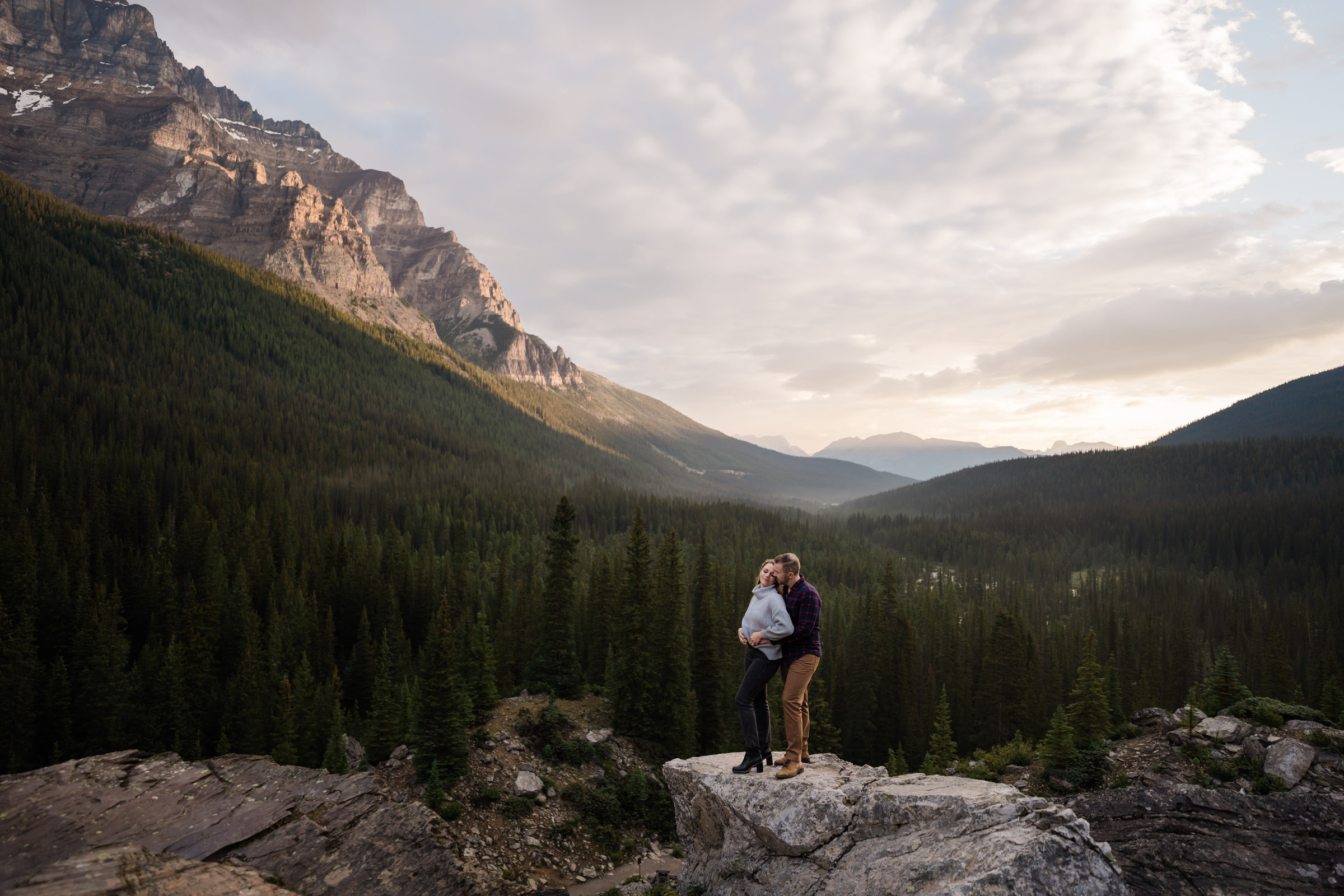 Couple holds each other as the sun lights up the valley behind them in Banff National Park.
