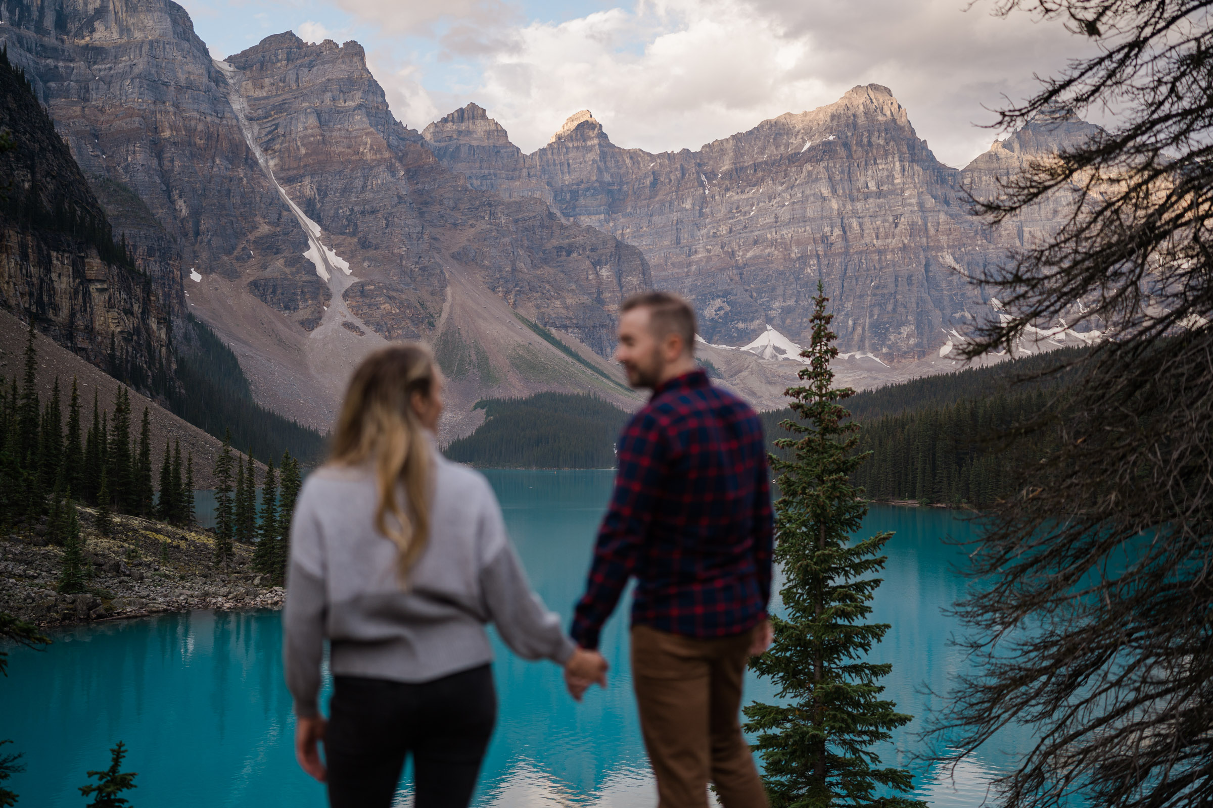 Couple holding hands and looking at each other out of focus and the sun comes up over Moraine Lake. 