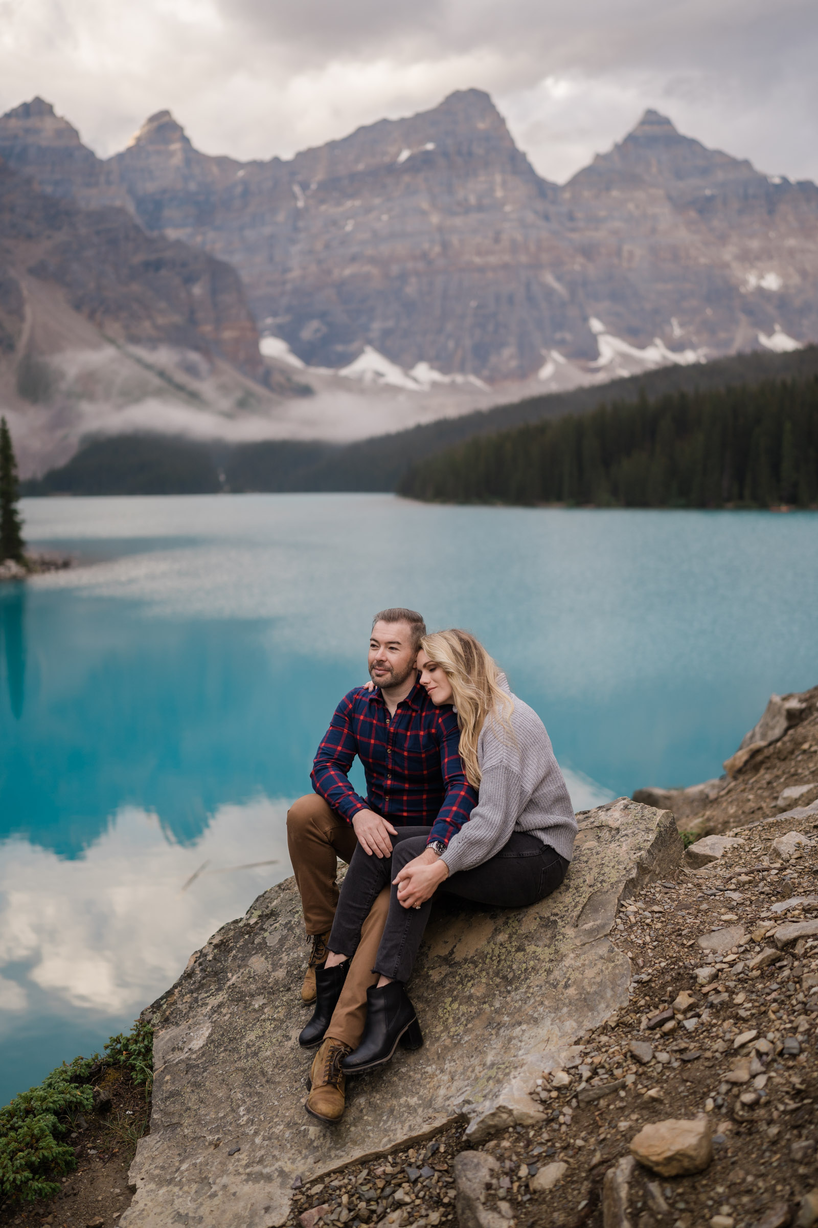 Couple sits on rock together while looking off into the distance during Banff engagement photos. 