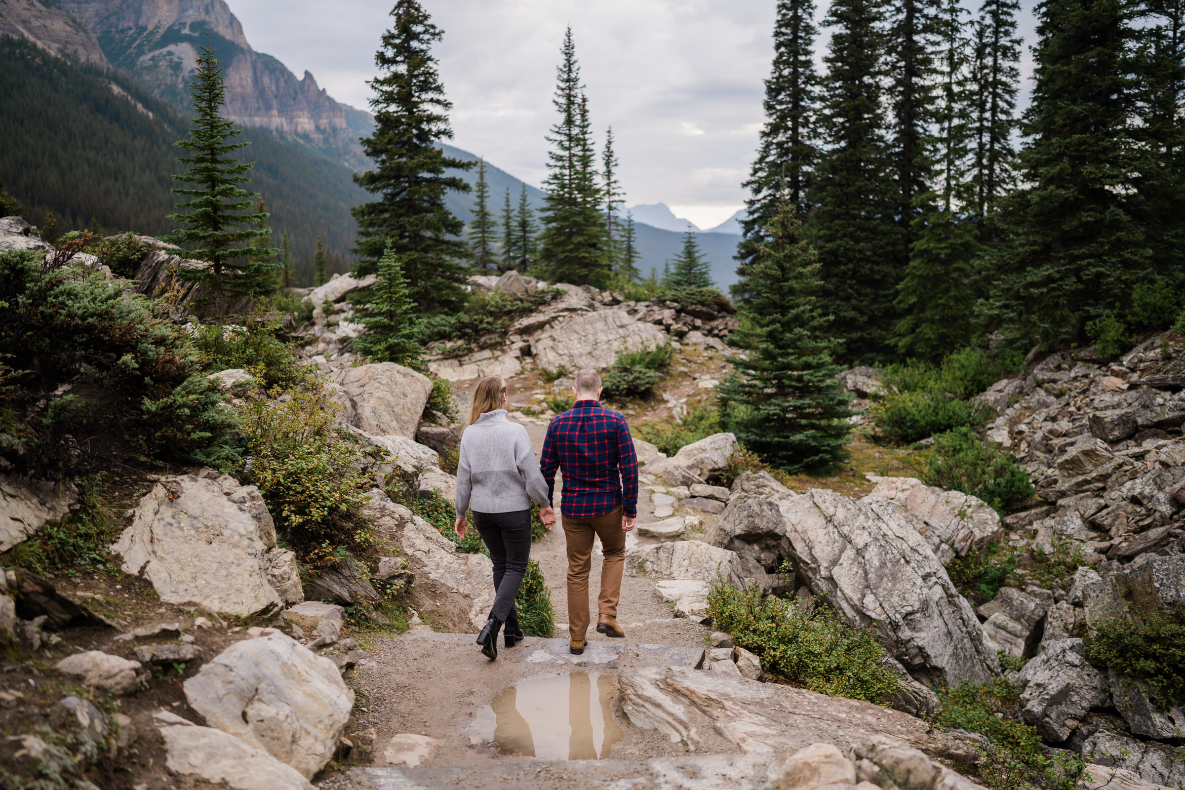 Couple hand in hand walks down the rockpile path at Moraine Lake. 