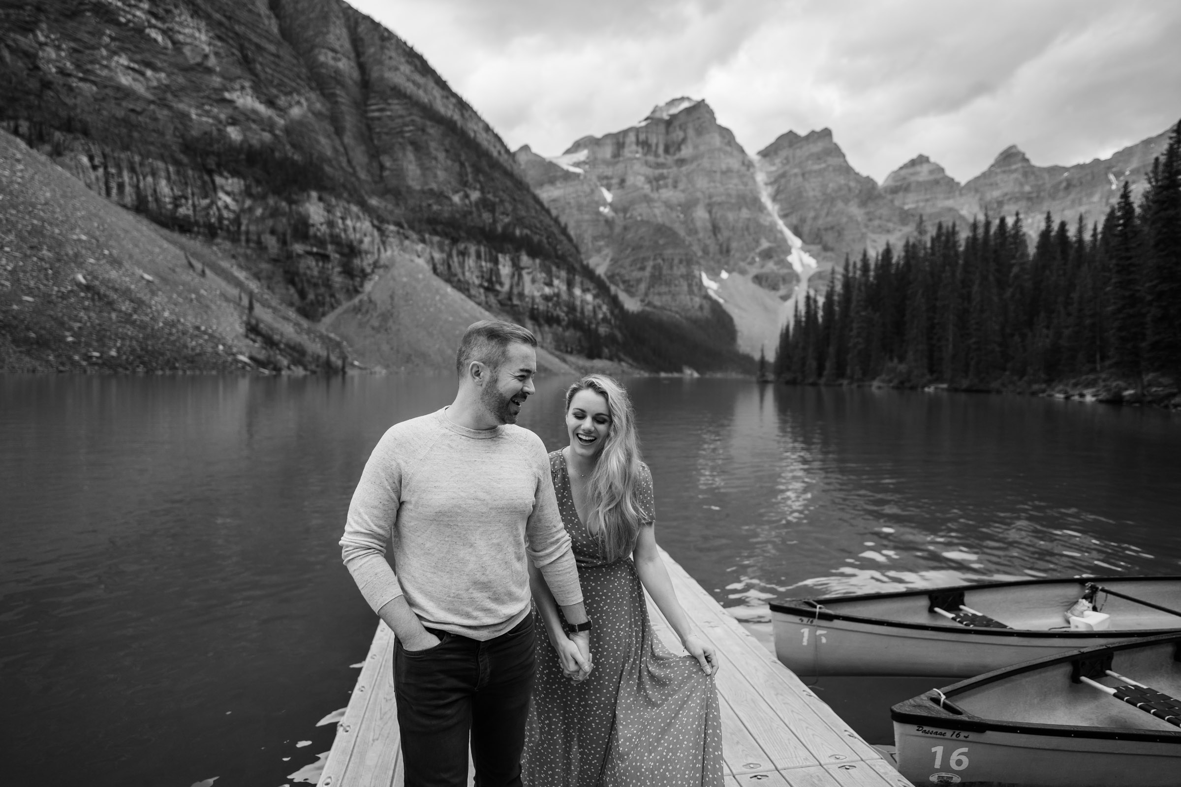 Black and white photo of fiances laughing on the dock at Moraine Lake. 