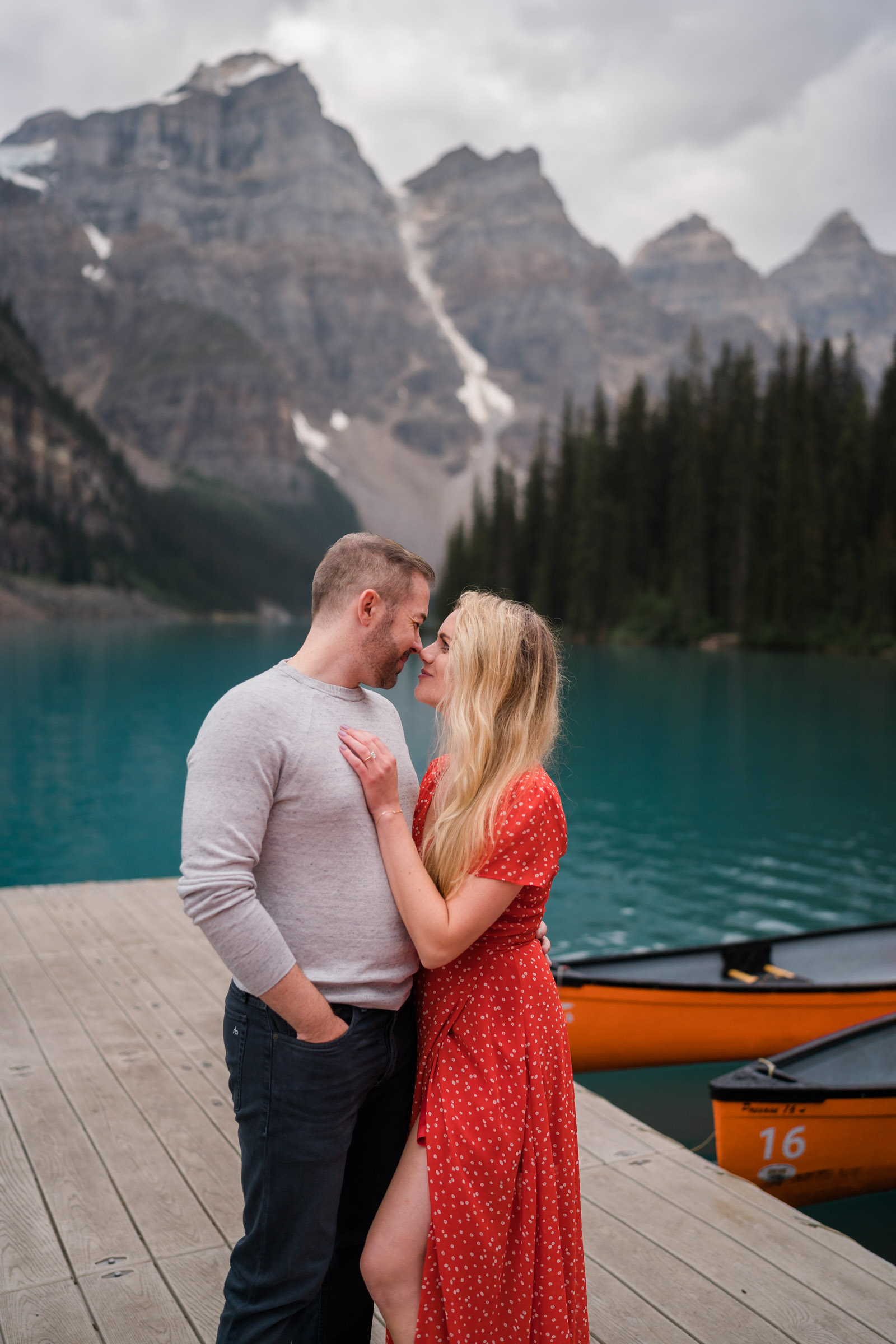 Woman in red dress gazes into her new fiances eyes on dock at Moraine Lake. 