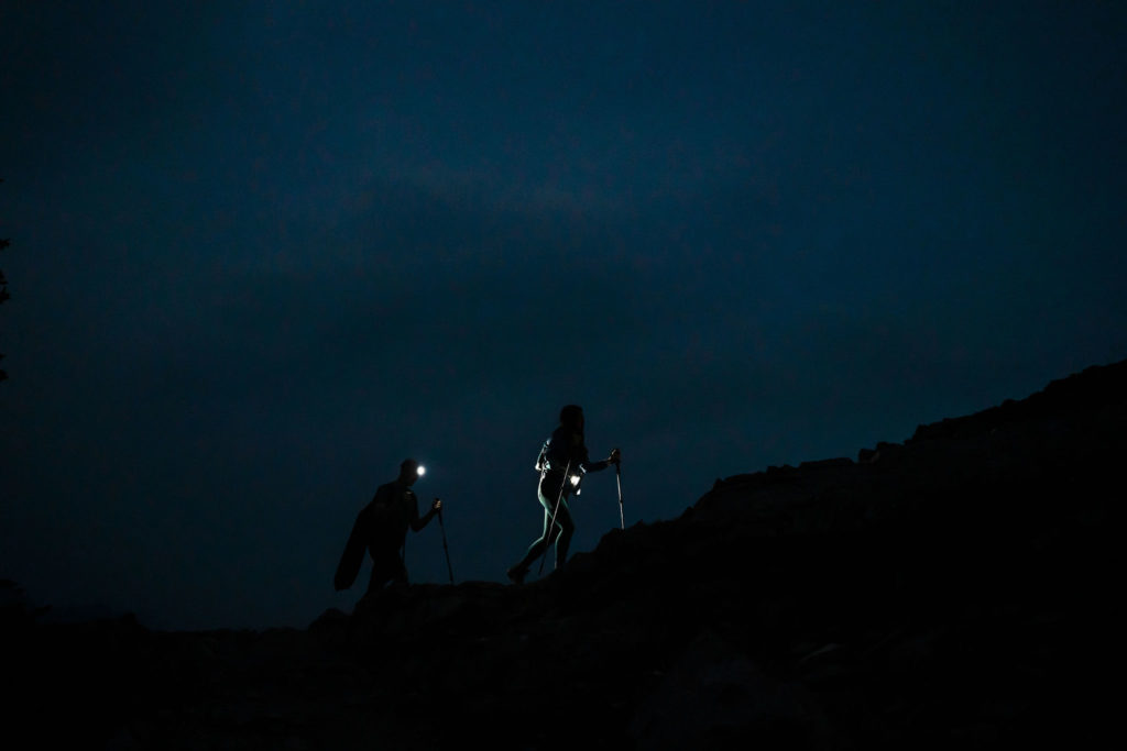 couple wearing headlamps hikes up a mountain in the dark with just their headlamps showing the way during their elopement