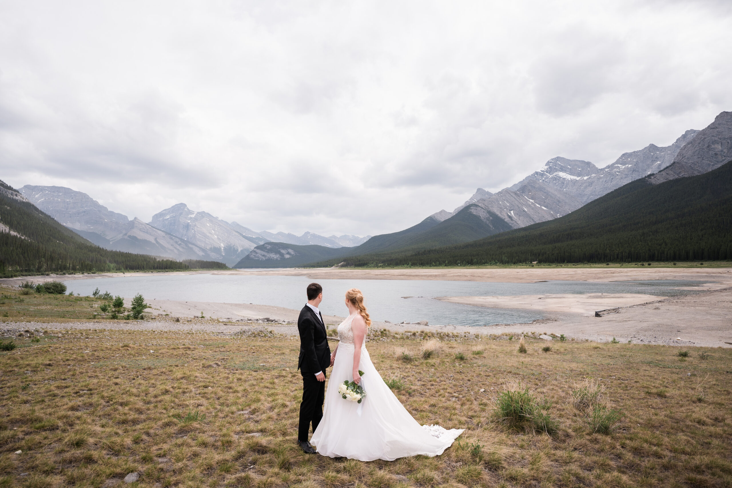 bride and groom hold hands and look down over spray lakes in kananaskis during elopement 