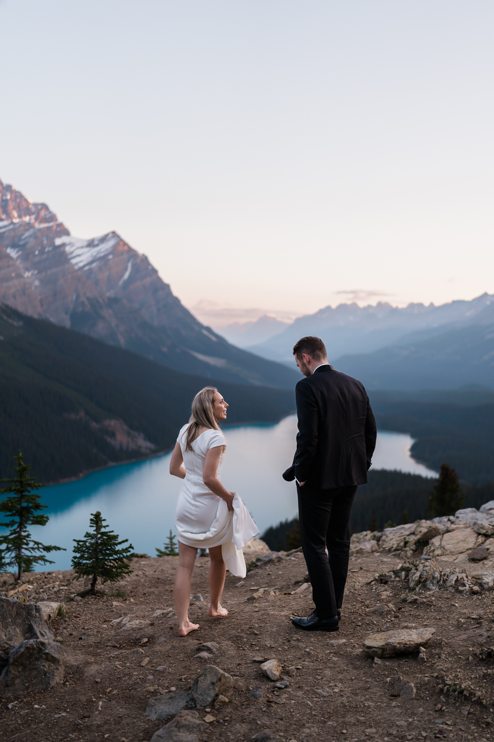 A barefoot bride walks beside the groom and they talk during their sunrise elopement in Banff National Park