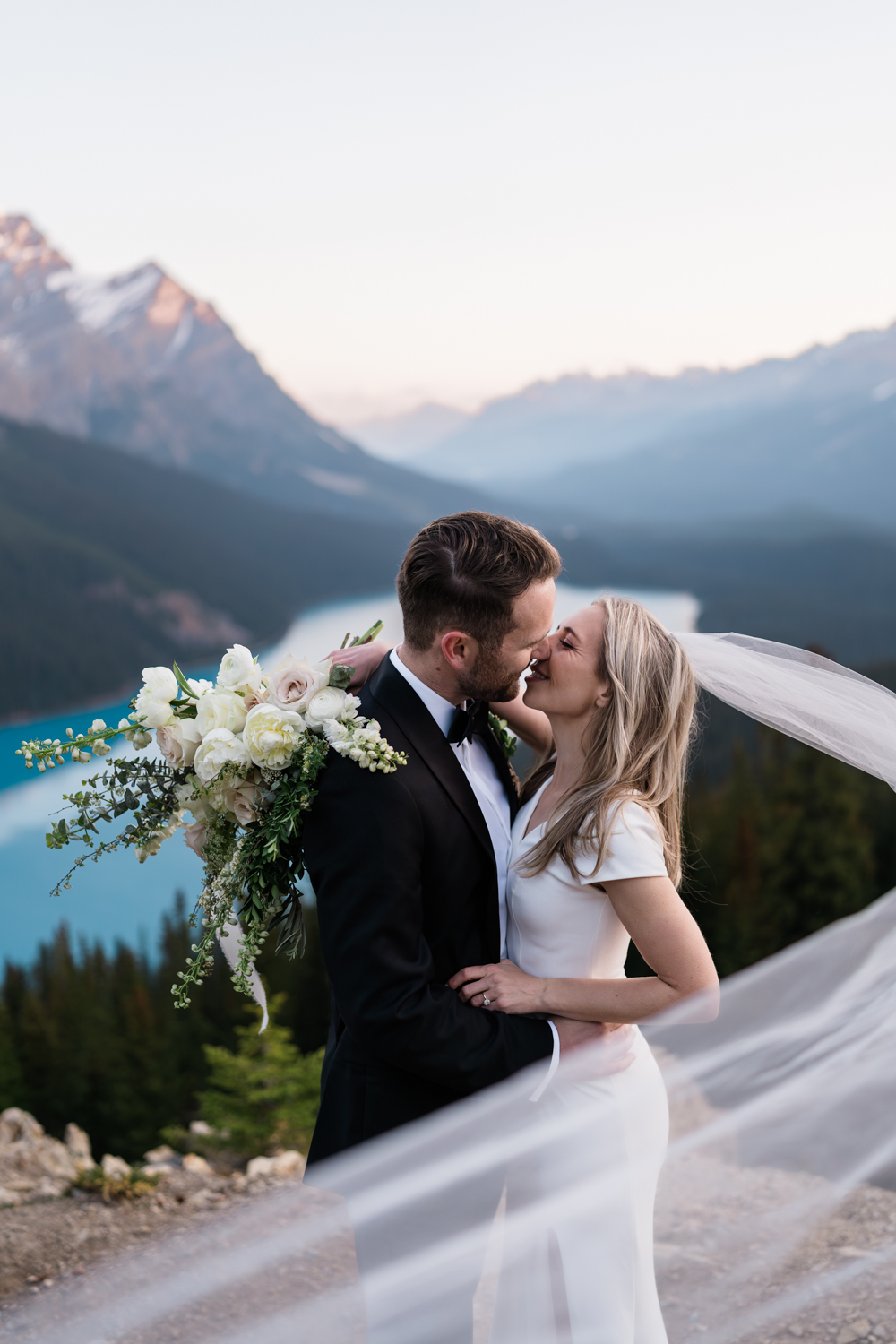 Couple who planned banff elopement kissing in front of Peyto Lake with veil blowing.