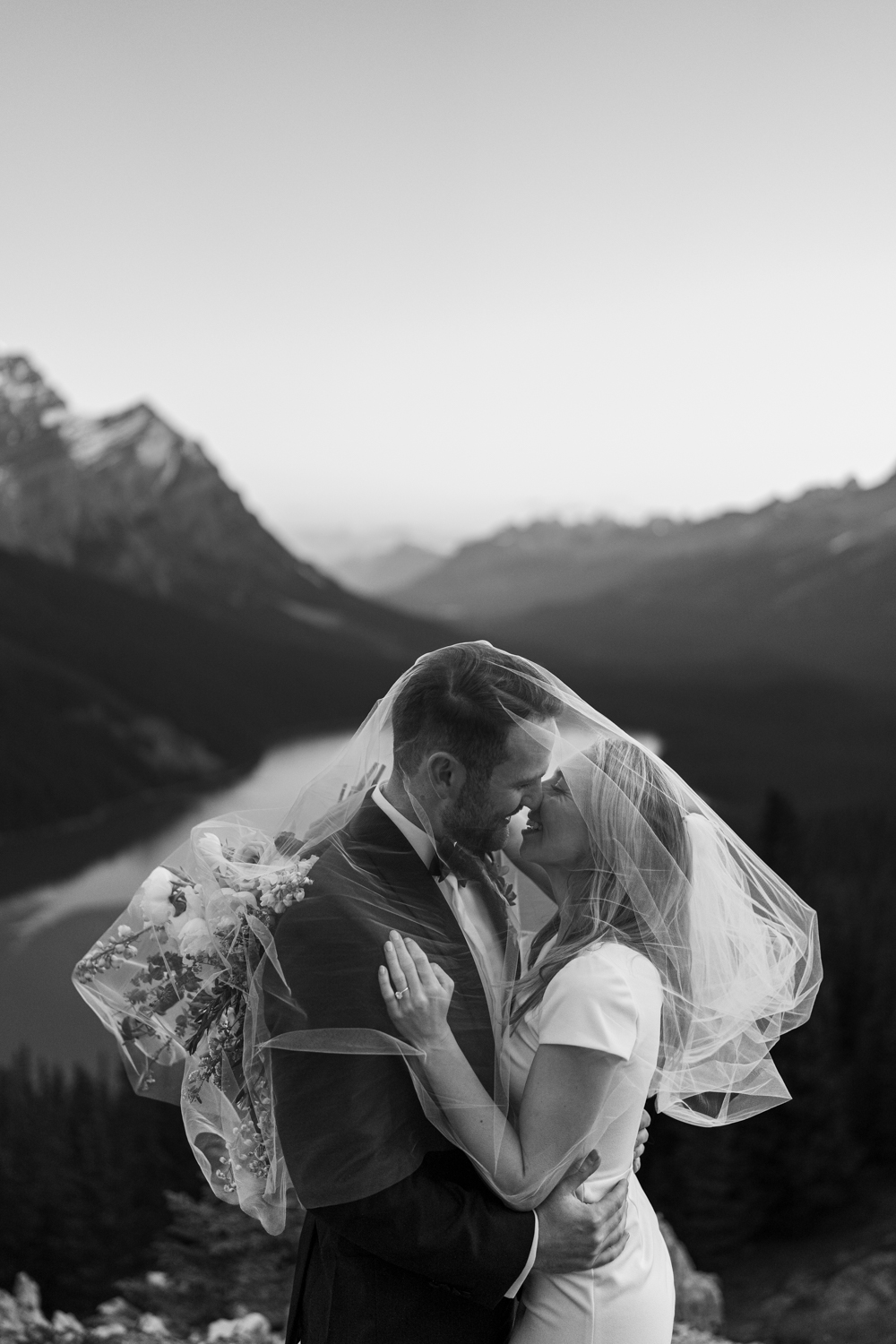 Black and white image of bride and groom kissing with veil wrapped around them
