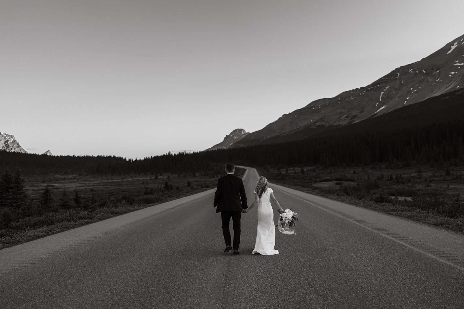 black and white photo of bride and groom walking down road on the  Icefields Parkway in Banff National Park during elopement