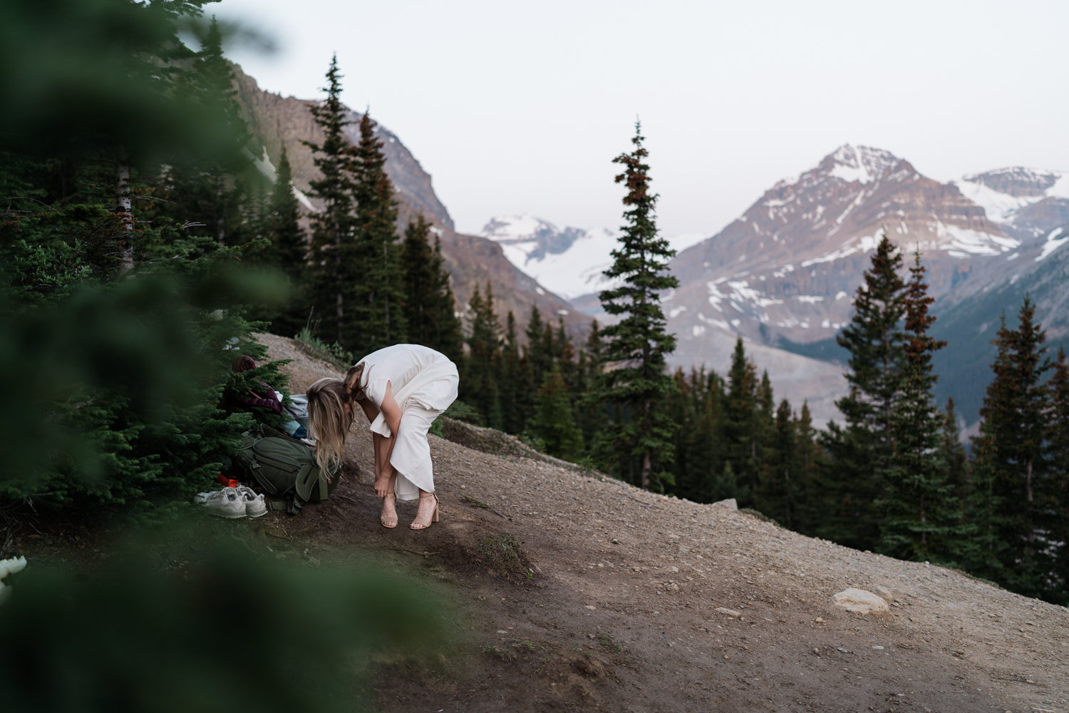 A bride puts on her heels on the side of a mountain before her sunrise banff elopement.
