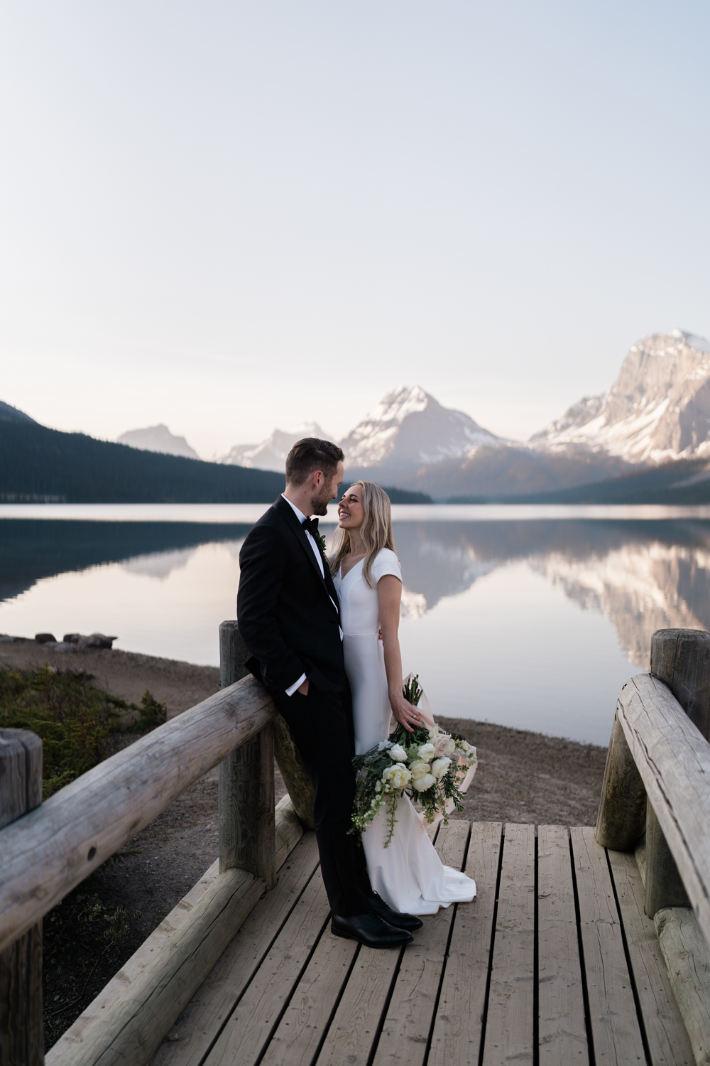 bride smiles at groom on bridge at Bow Lake in Banff National Park at sunrise