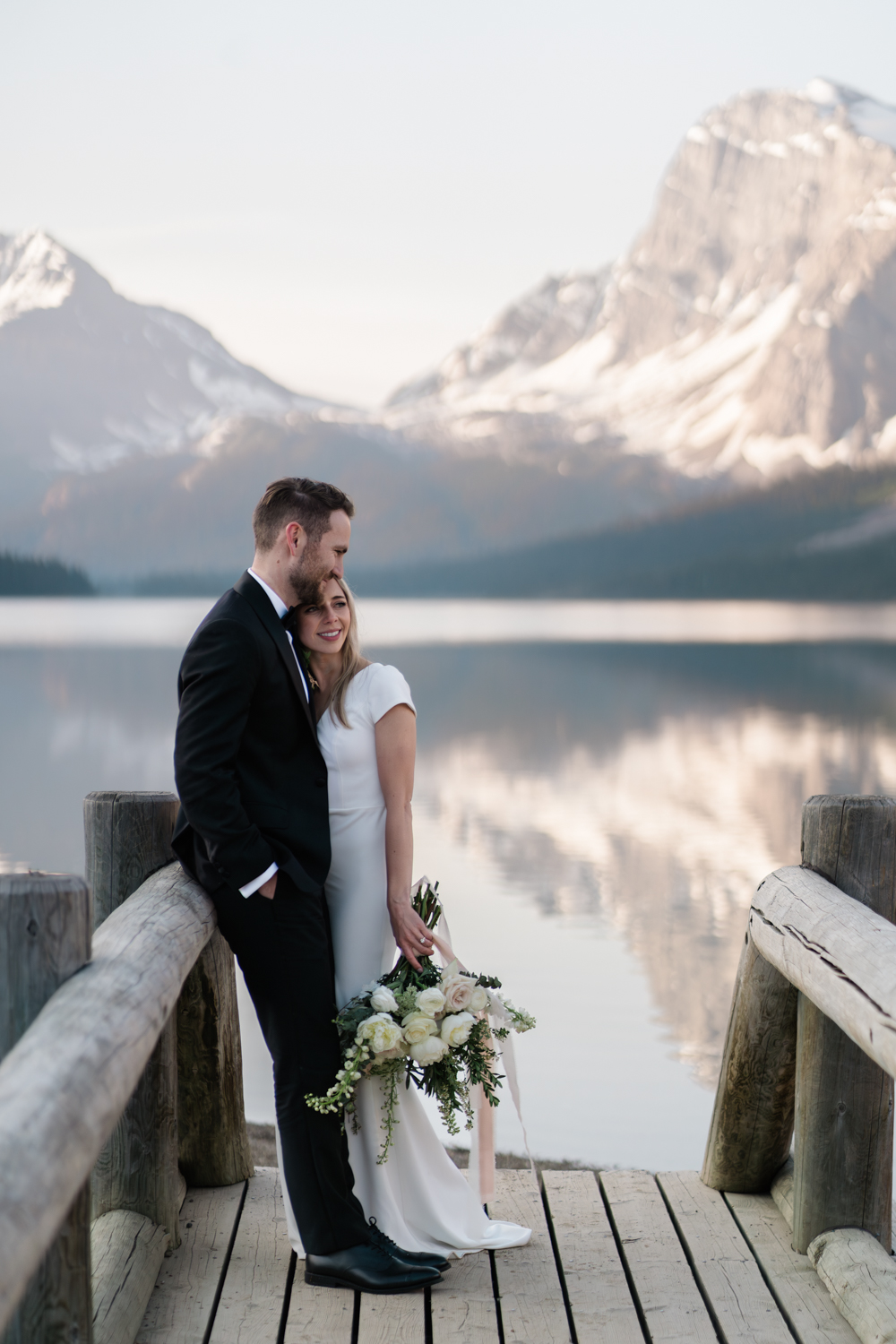 bride and groom snuggle on the bridge at Bow Lake in Banff National Park at sunrise for their elopement