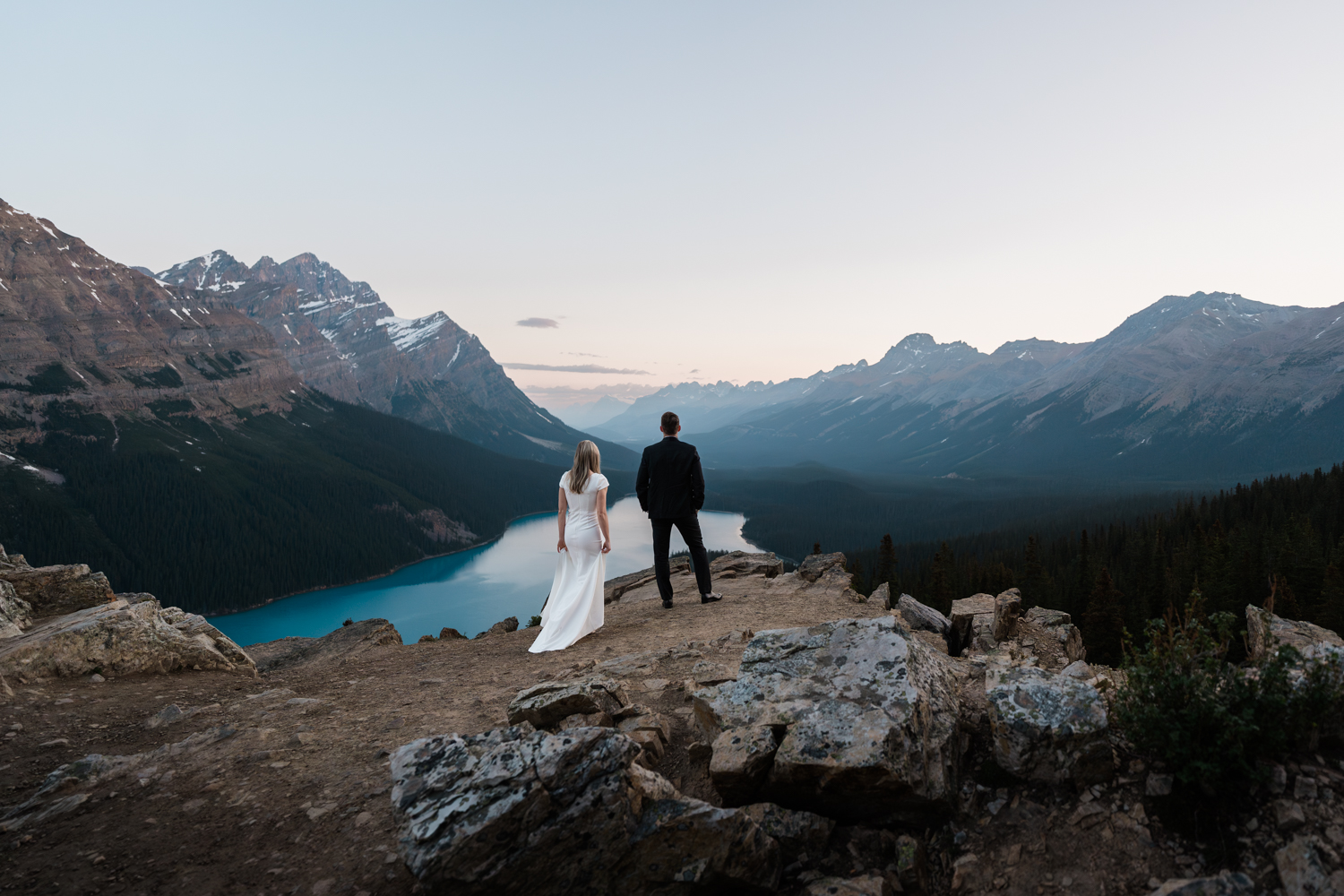 bride walks up behind the groom who is looking out over Peyto Lake in Banff National Park