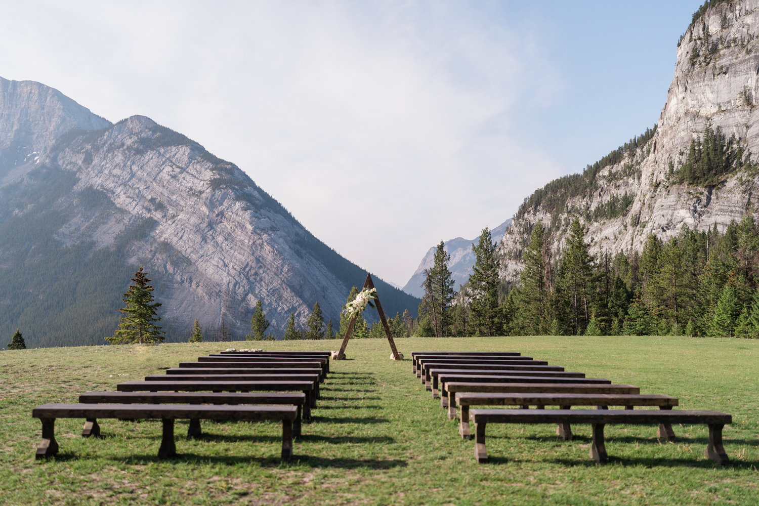 Tunnel Mountain in Banff wedding ceremony set up with triangle arch with flowers and rows of wood bench seating