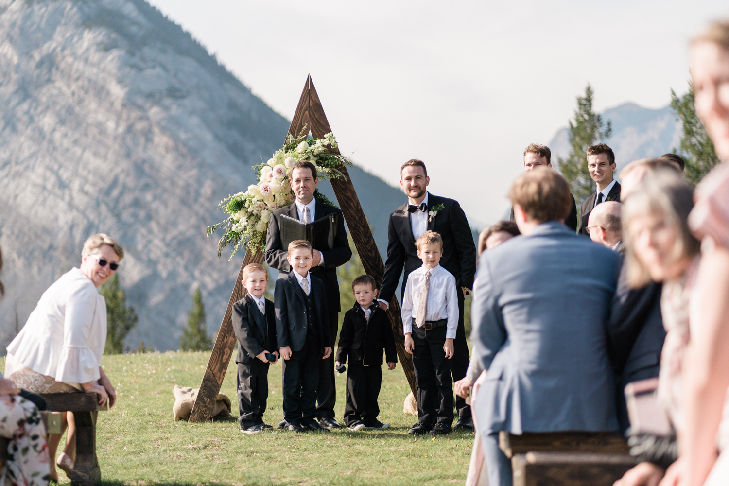 groom stands at head of aisle at Tunnel Mountain in Banff with group of young bows infront of him waiting for the bride