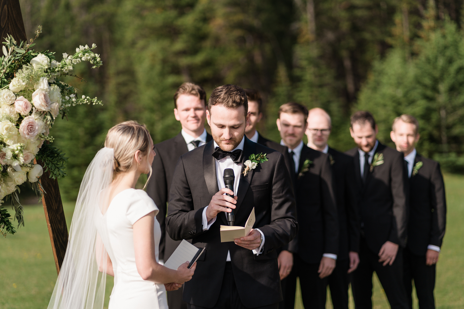 groom holds microphone and looks down at his vow booklet while reading his vows during ceremony at Tunnel Mountain in Banff 