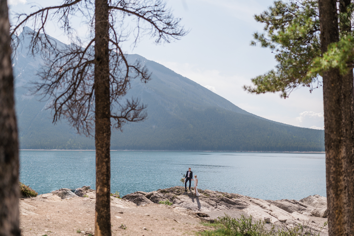 bride and groom stand on rocks at Lake Minnewanka in Banff National Park