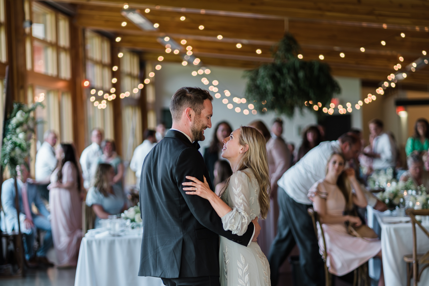 bride and groom have first dance and look at each other with guests and twinkly lights behind them at Fenlands in Banff 