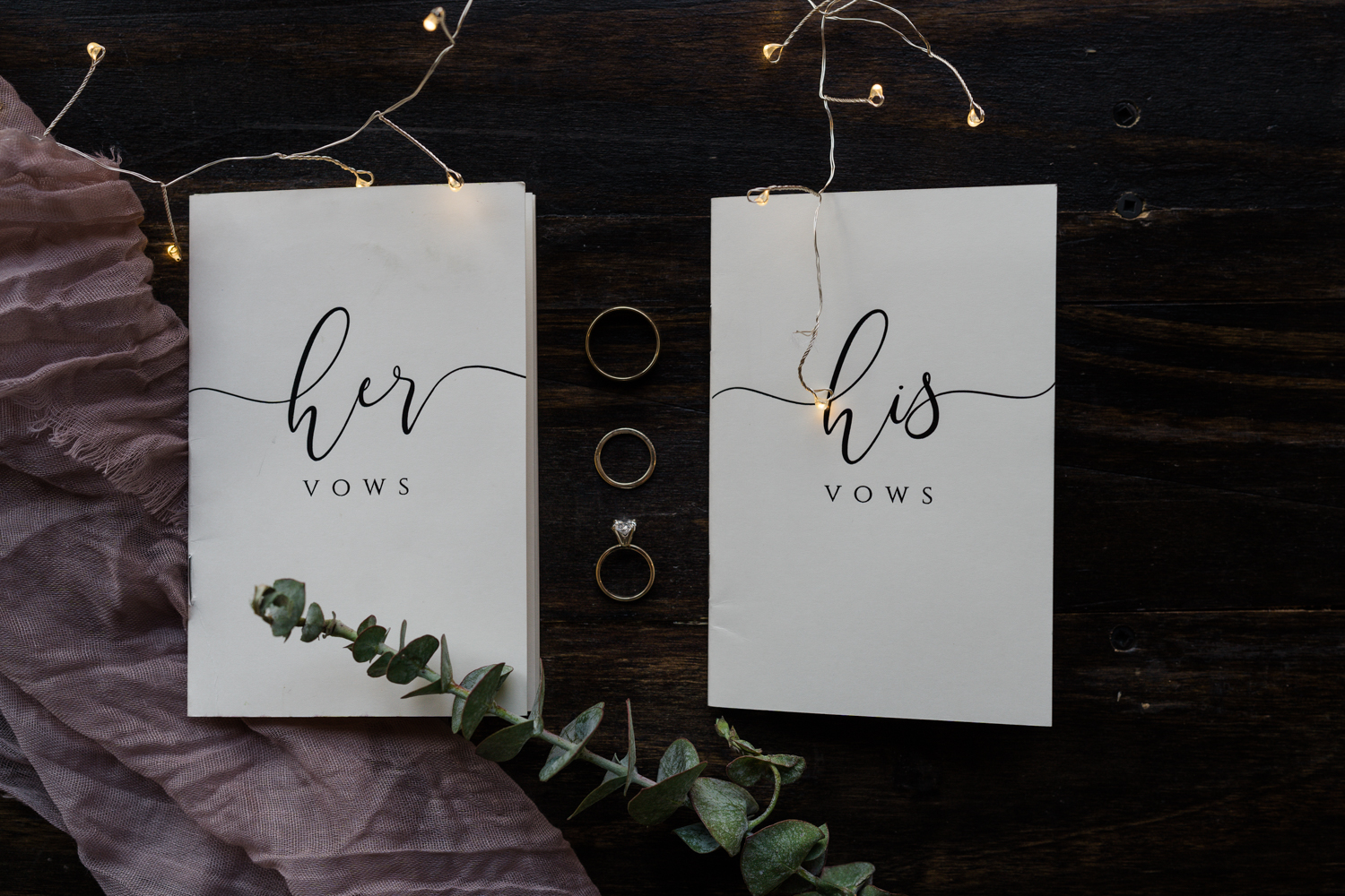 his and hers vow booklets with the rings and greenery and twinkly lights surrounding it in Banff National Park