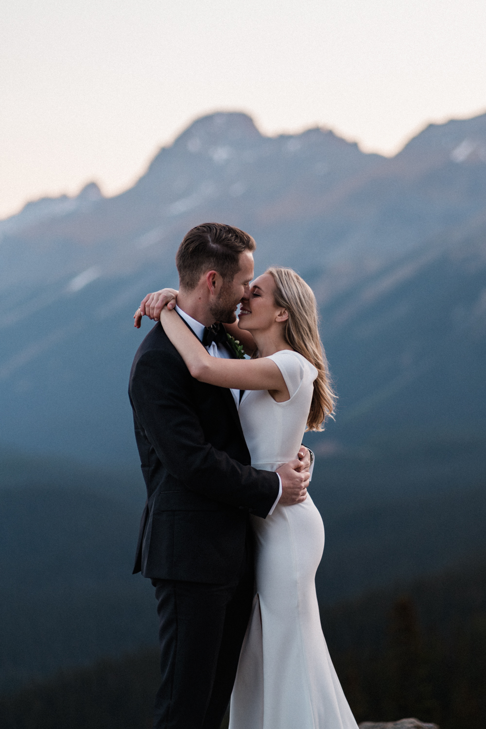 Bride and groom embrace infront of mountains as the sun comes up 