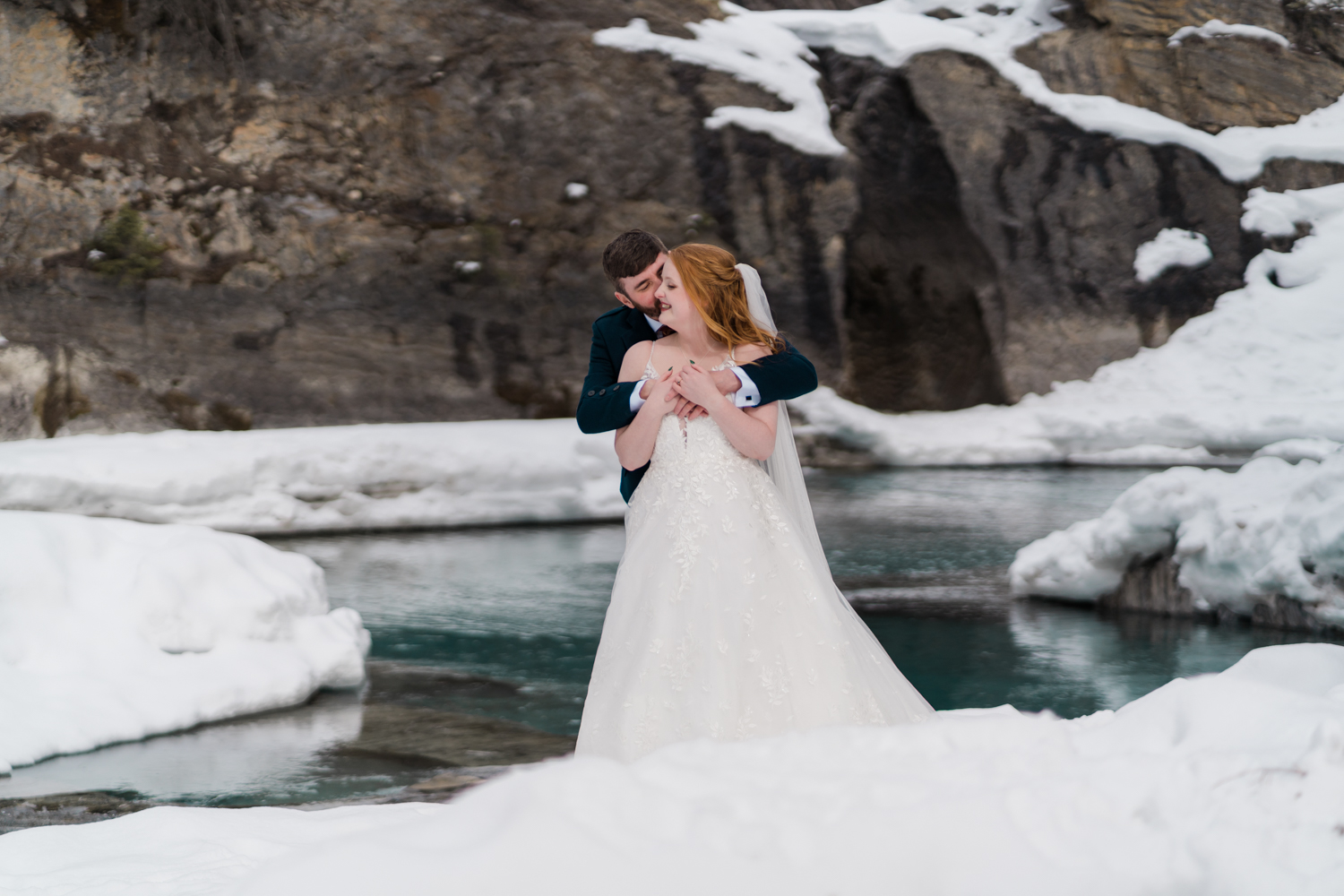 groom nuzzles into brides neck with the blue water of the Kicking Horse River behind them