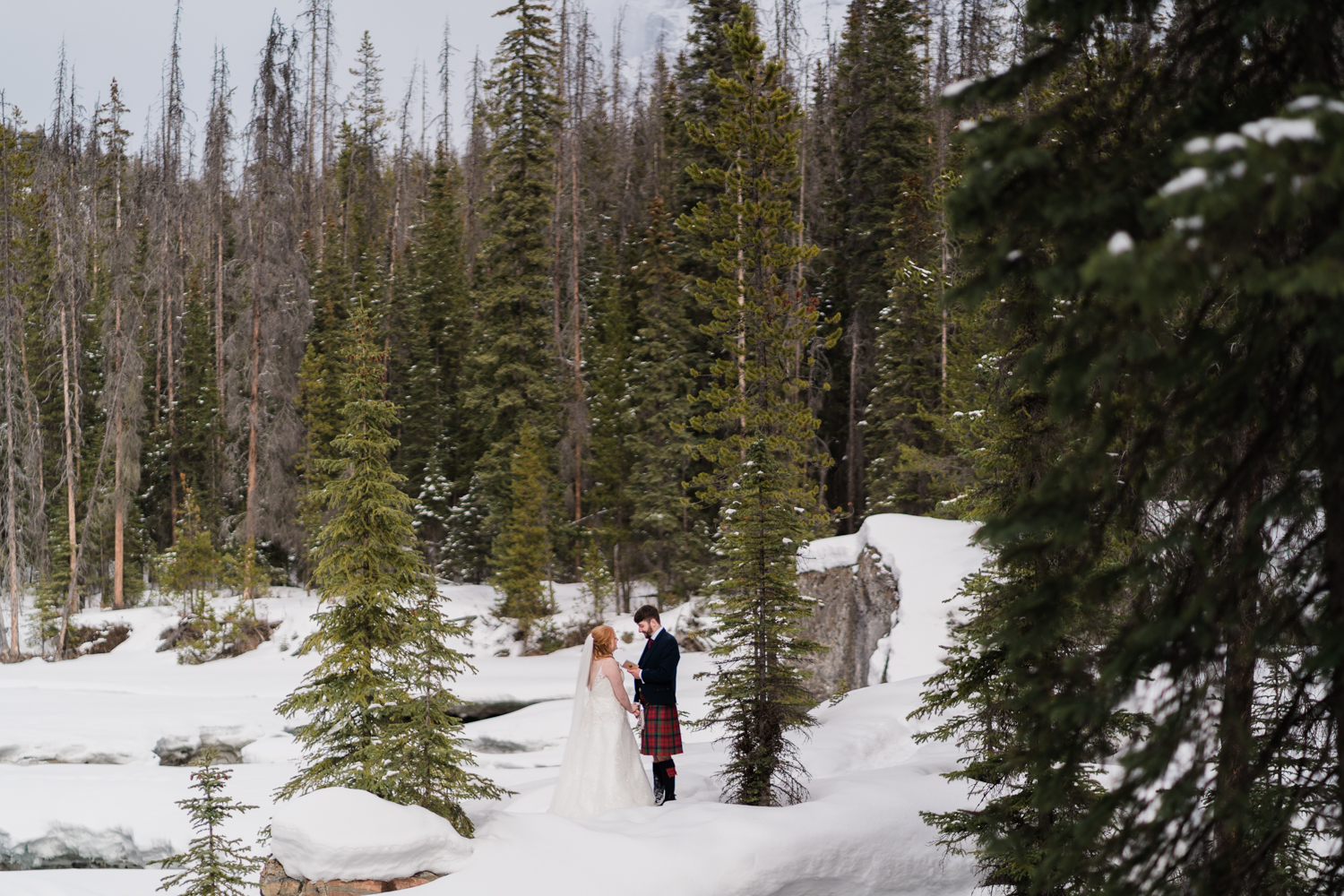 a groom in a kilt says his vows to his bride in a snowy forest in yoho national park
