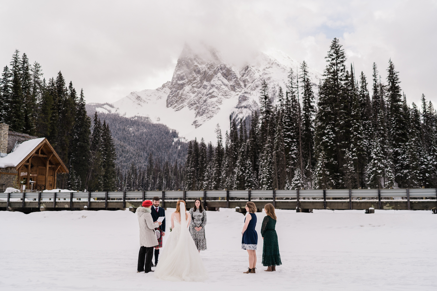 a small wedding on the frozen Emerald Lake with the lodge and mountain in the background