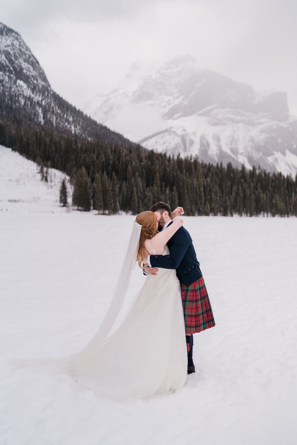 bride and groom kiss on a snow covered lake with the mountains in the background during their Emerald Lake elopement