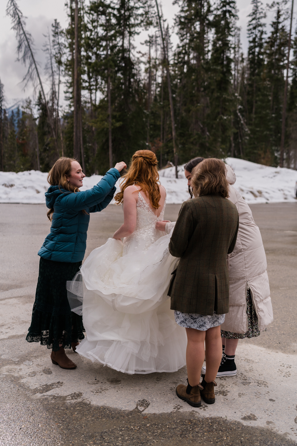 Bride gets ready with her three friends doing up her dress and fixing her hair in the parking lot for her Emerald Lake elopement