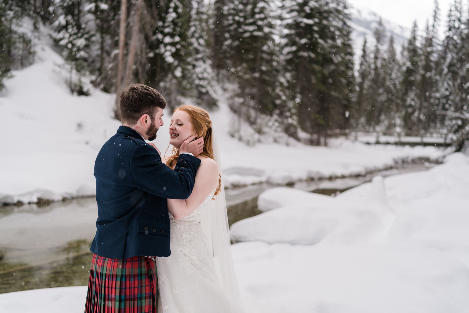 groom holds brides face as she smiles at him with the snow falling during an Emerald Lake elopement