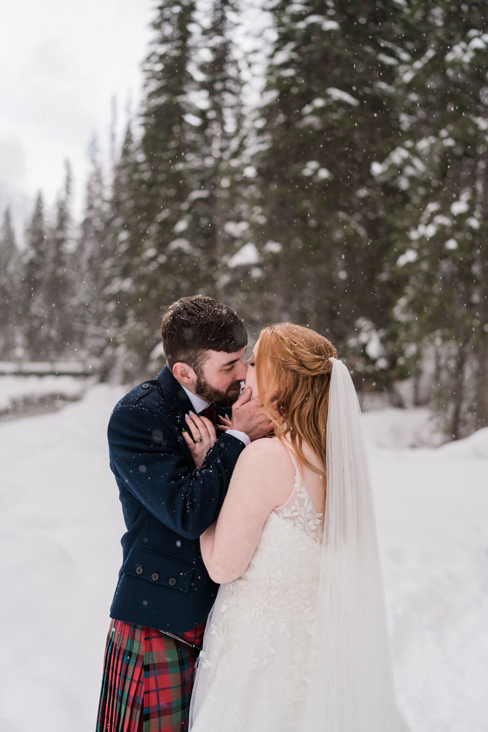 close up of the snow falling down around a bride and groom in a kilt while they kiss