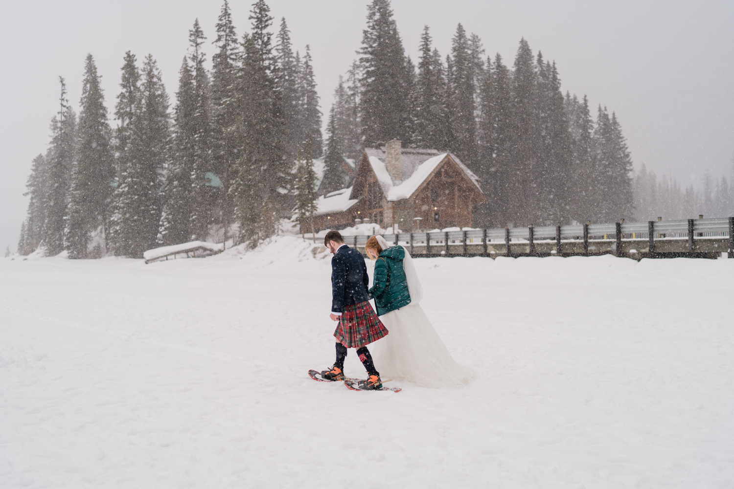 Bride and groom snowshoe in front of Emerald Lake Lodge in a snowstorm