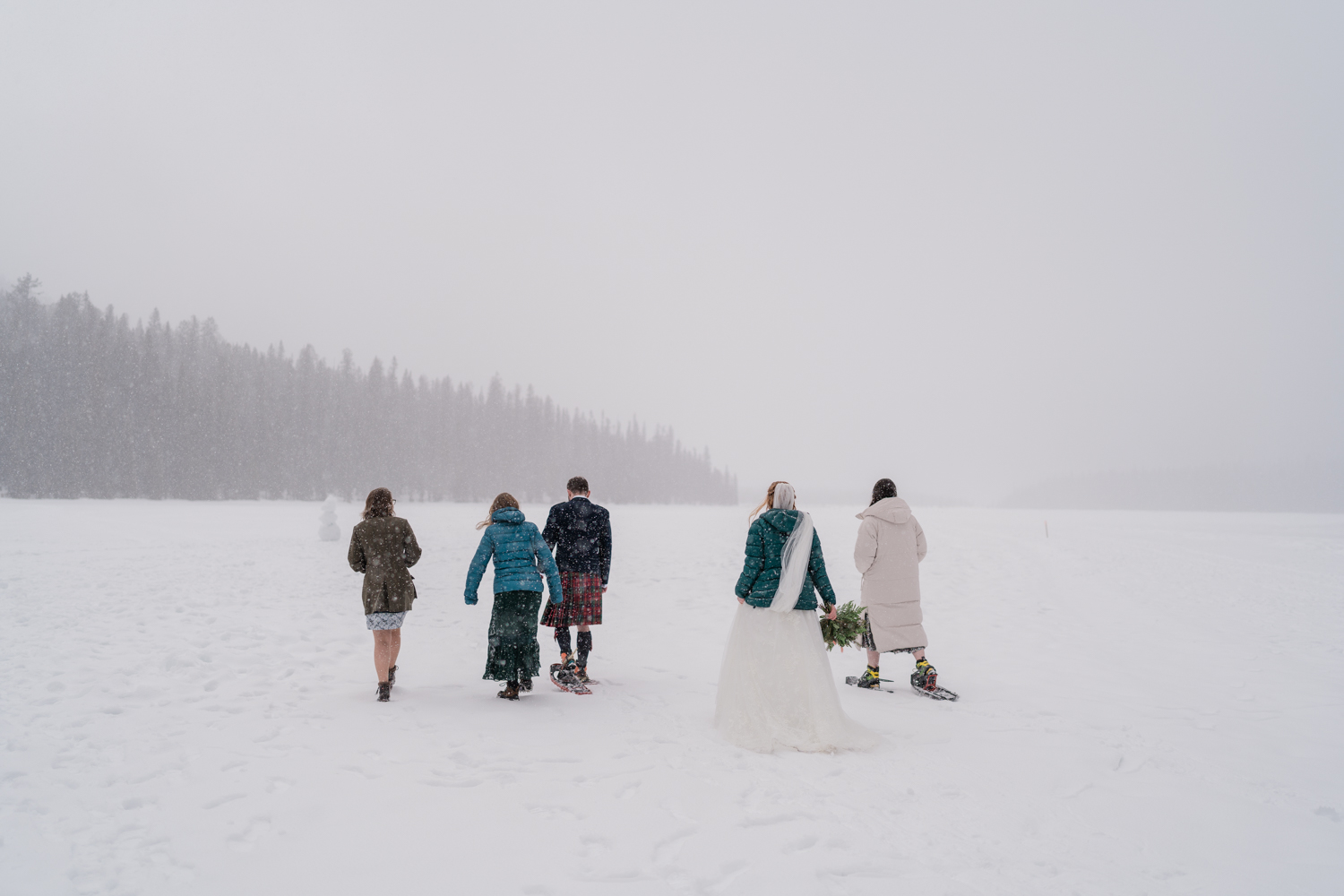 Bride and groom and 3 friends snowshoe off into the distance on a frozen Emerald Lake in a snowstorm