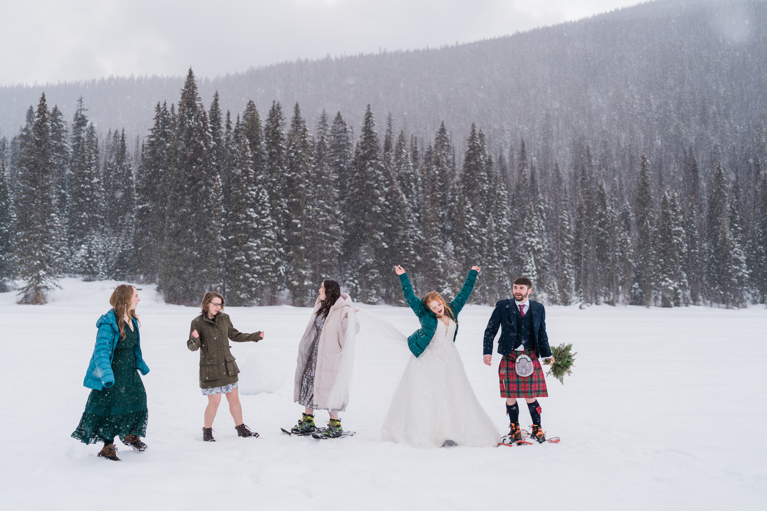 Bride and groom and 3 friends dance in a snowstorm during their emerald Lake elopement