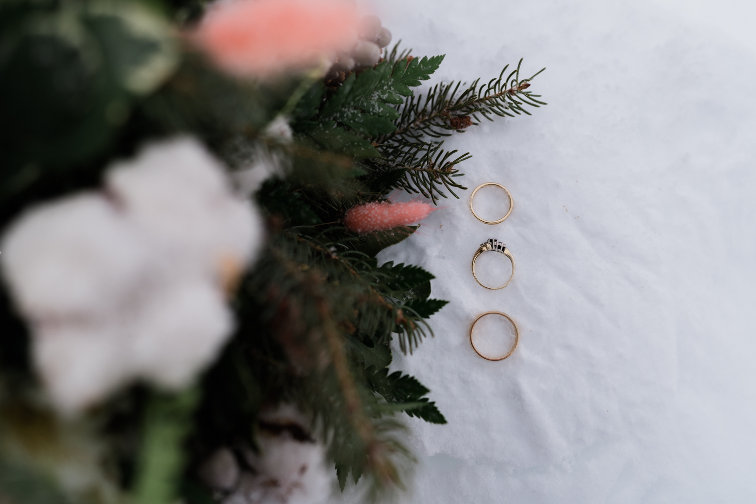 three golden rings sit on the snow with the bouquet beside them during a winter emerald lake elopement
