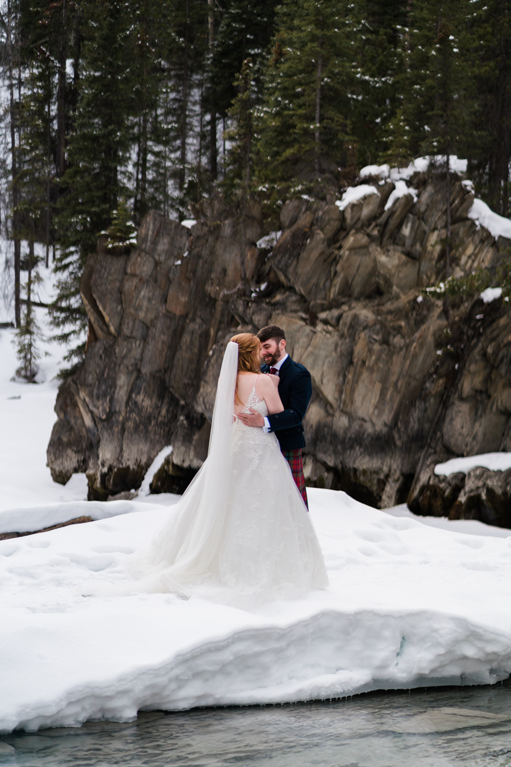 close up of bride and groom embracing while standing on snowy ground with a rockface in the background