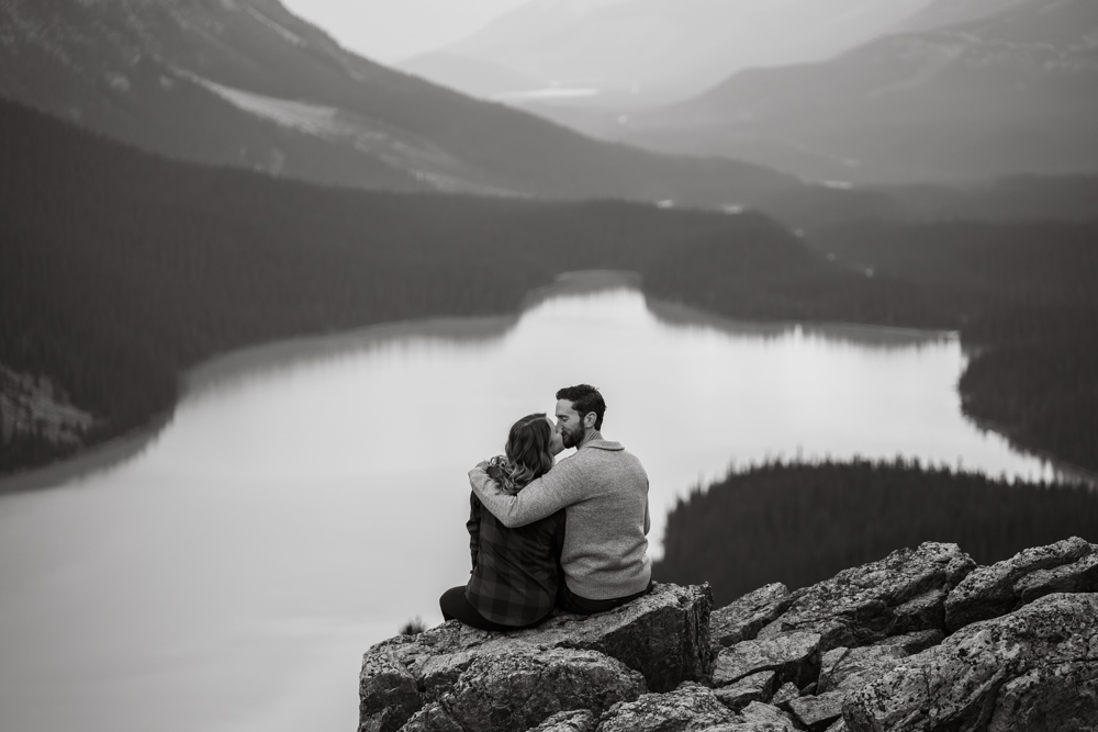 black and white photo of a couple sitting on the rocks over Peyto Lake as they kiss with the lake behind them